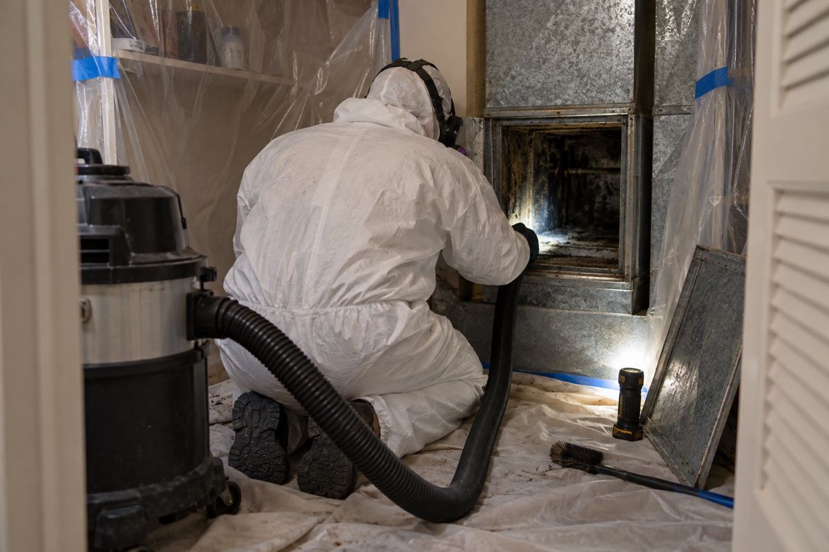 Worker in protective gear containing a stained duct section in a closet